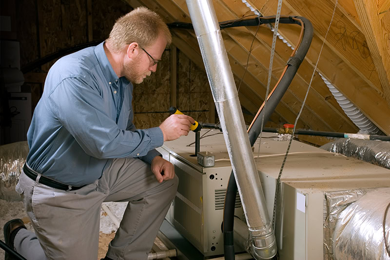 HVAC Technician performing maintenance on a furnace installed in an attic.
