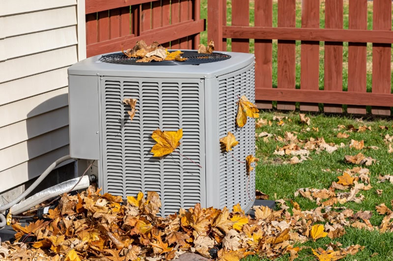Fall leaves surrounding an HVAC unit installed outside of a home.